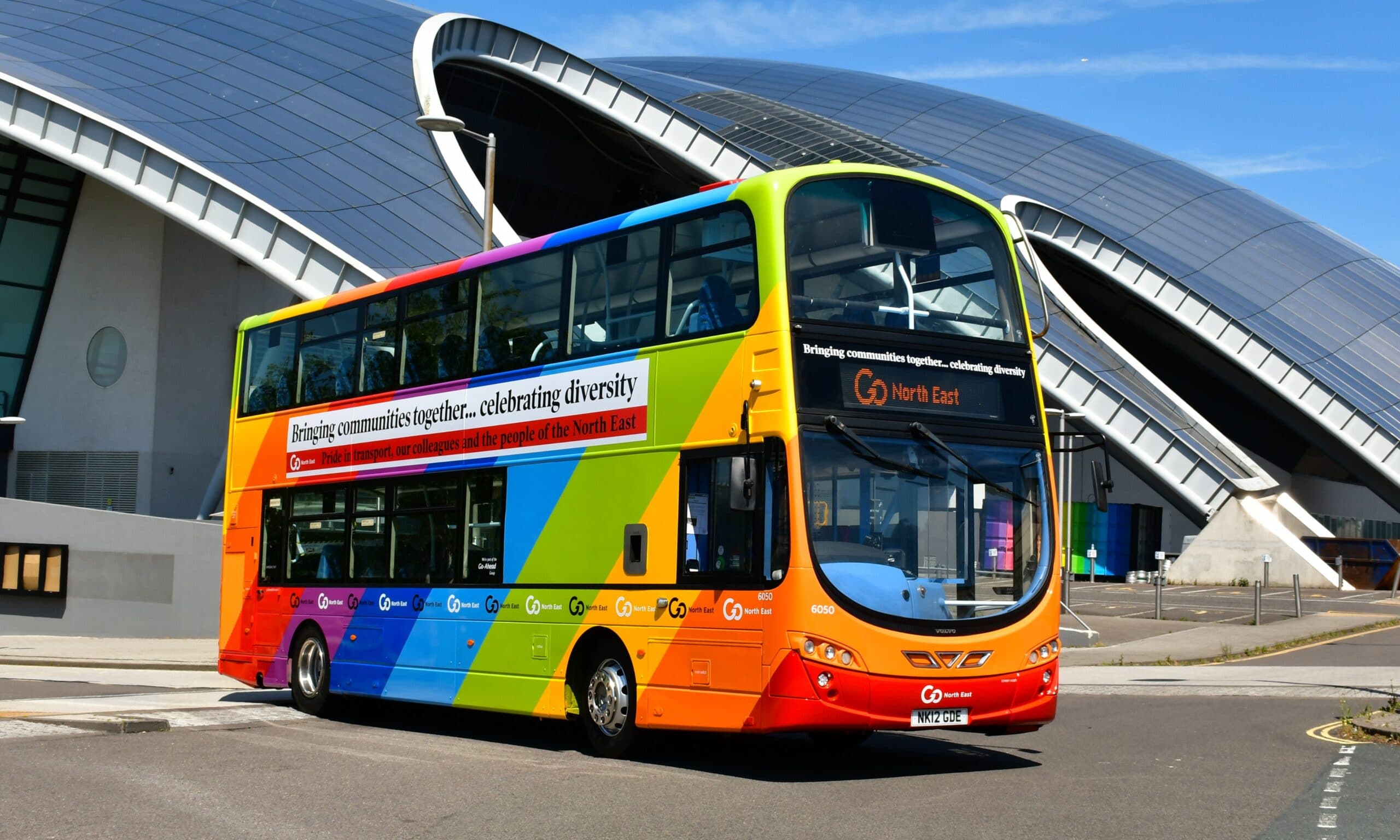 Go North East bus pained in rainbow colours under a large silver building