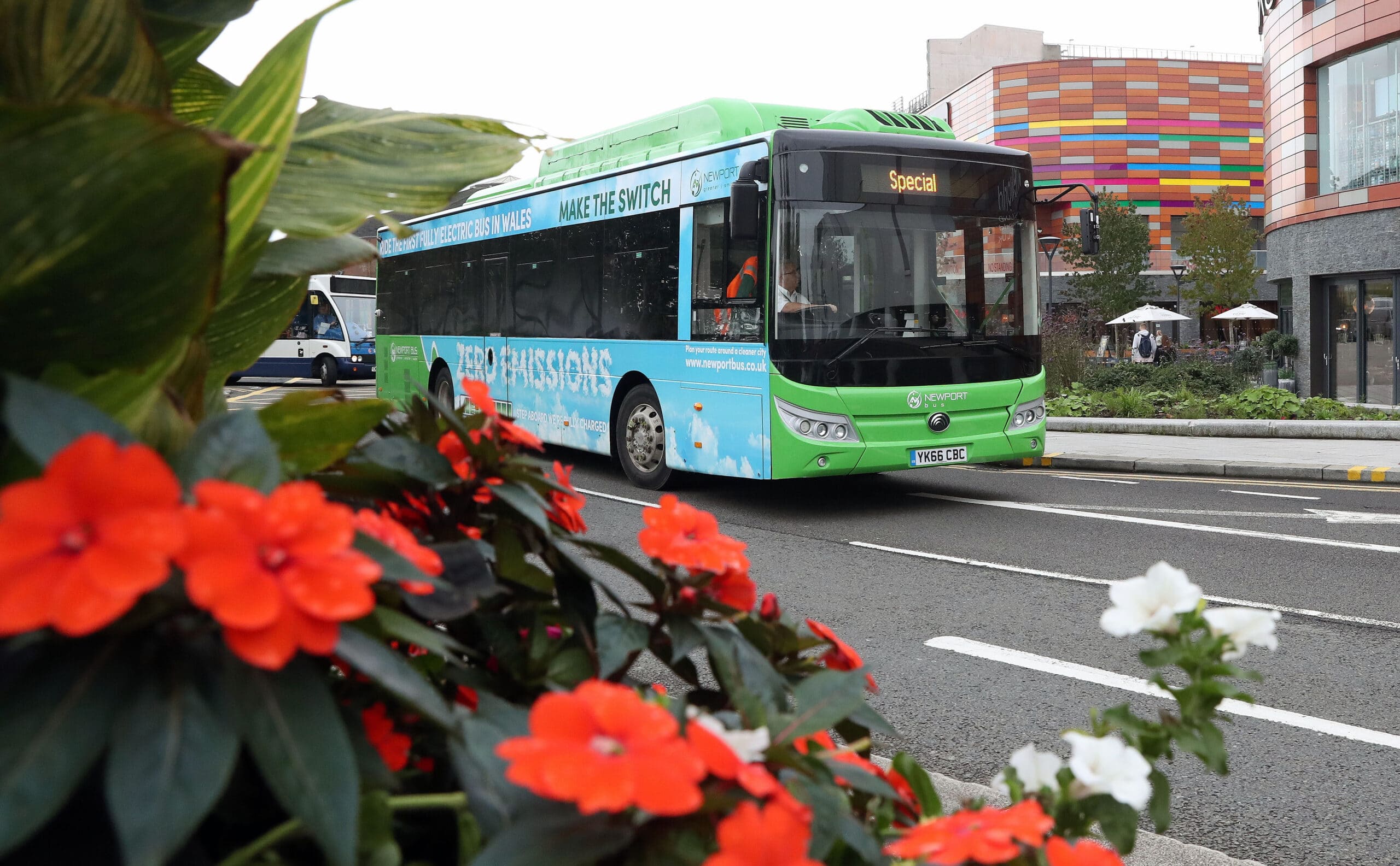 Newport Bus electric bus travelling down a road lined with flowers.