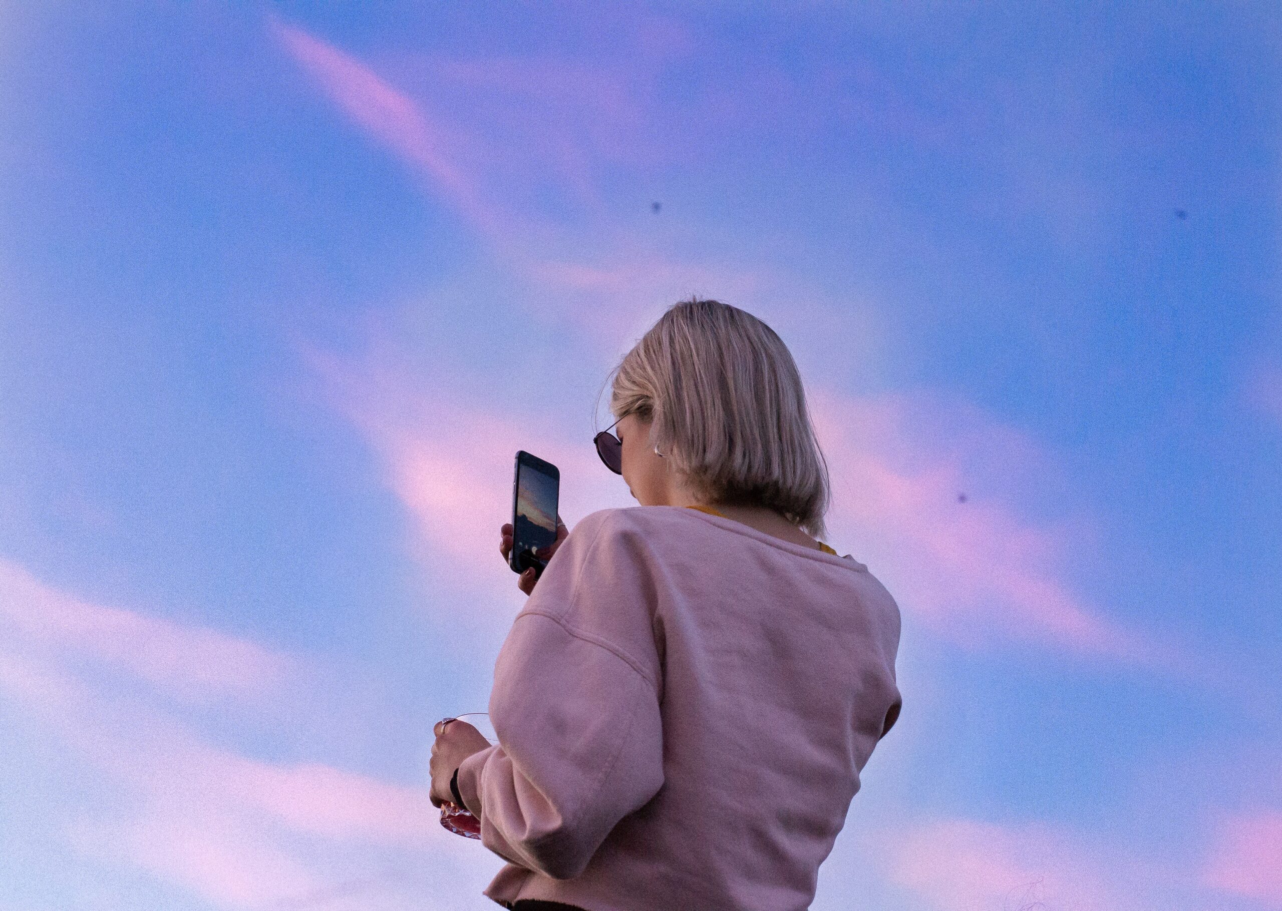 Person holding a mobile phone up with a sunset behind them