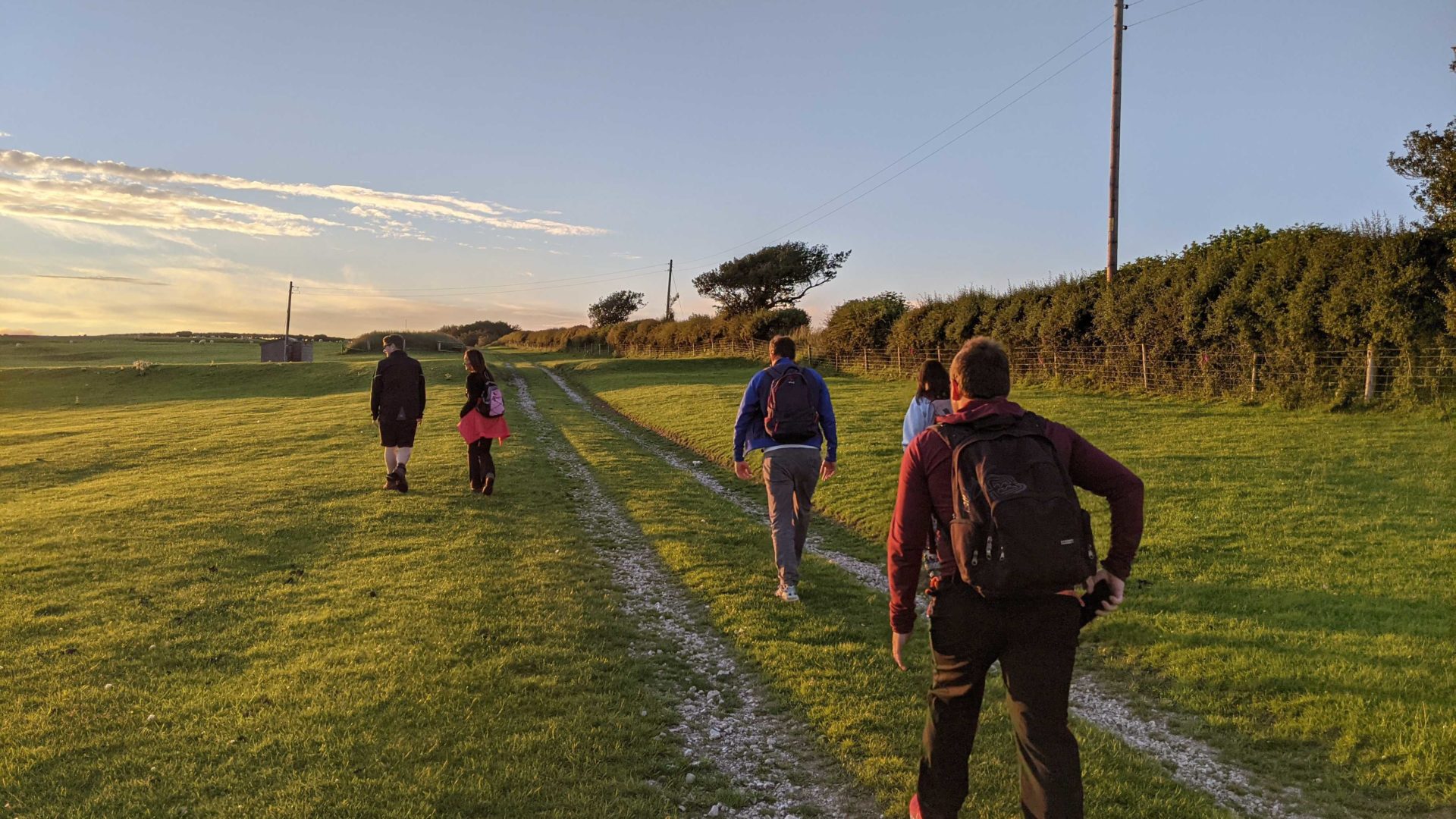 A group of people following a path through a country field at sunset.