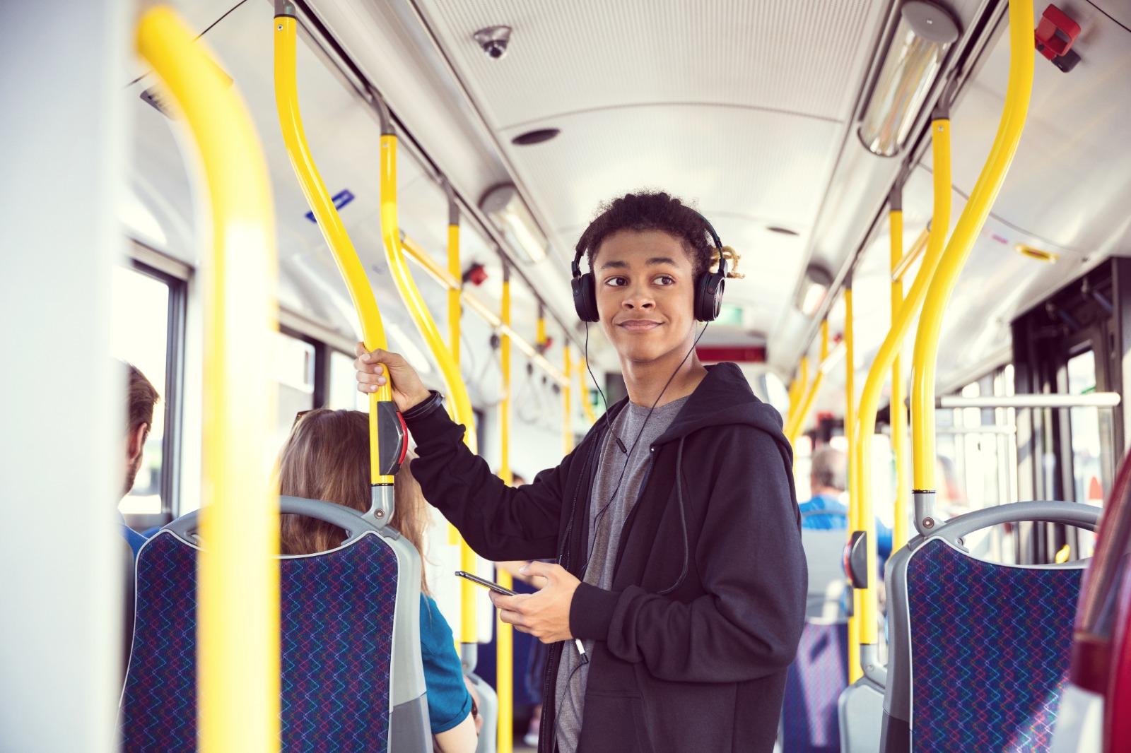 Person standing on a bus holding a phone, with headphones on. They are smiling.