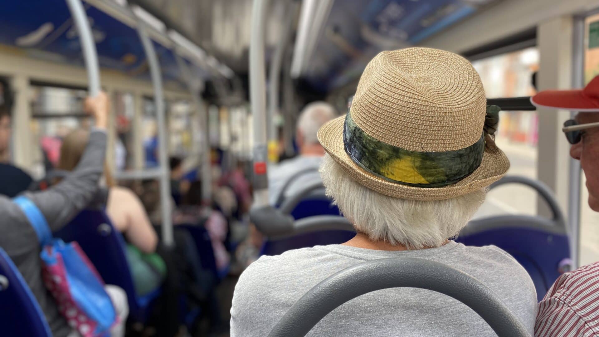 An older, fashionable lady sitting at the back of a busy single decker bus.