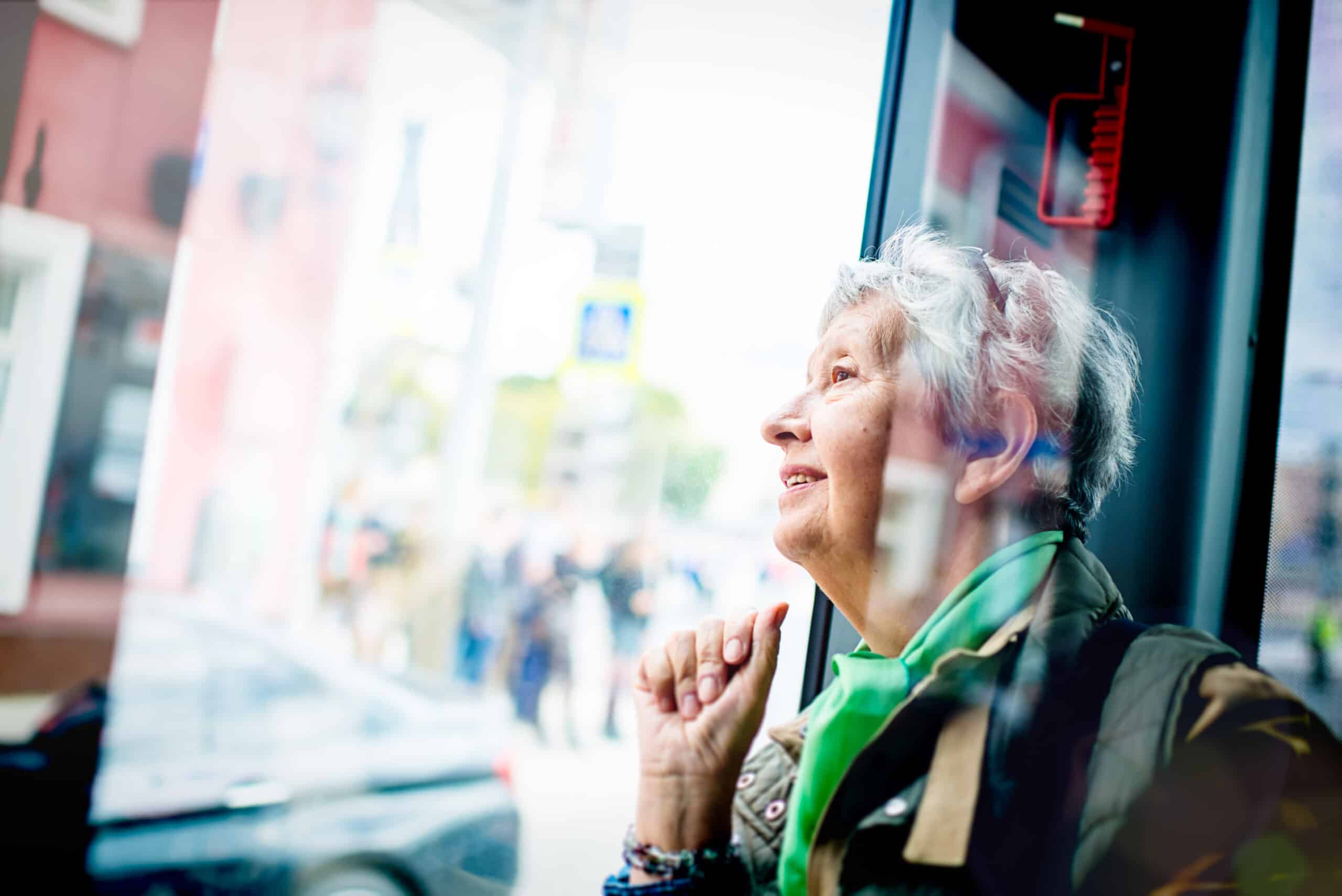 Senior woman sitting on a bus looking out of the window smiling