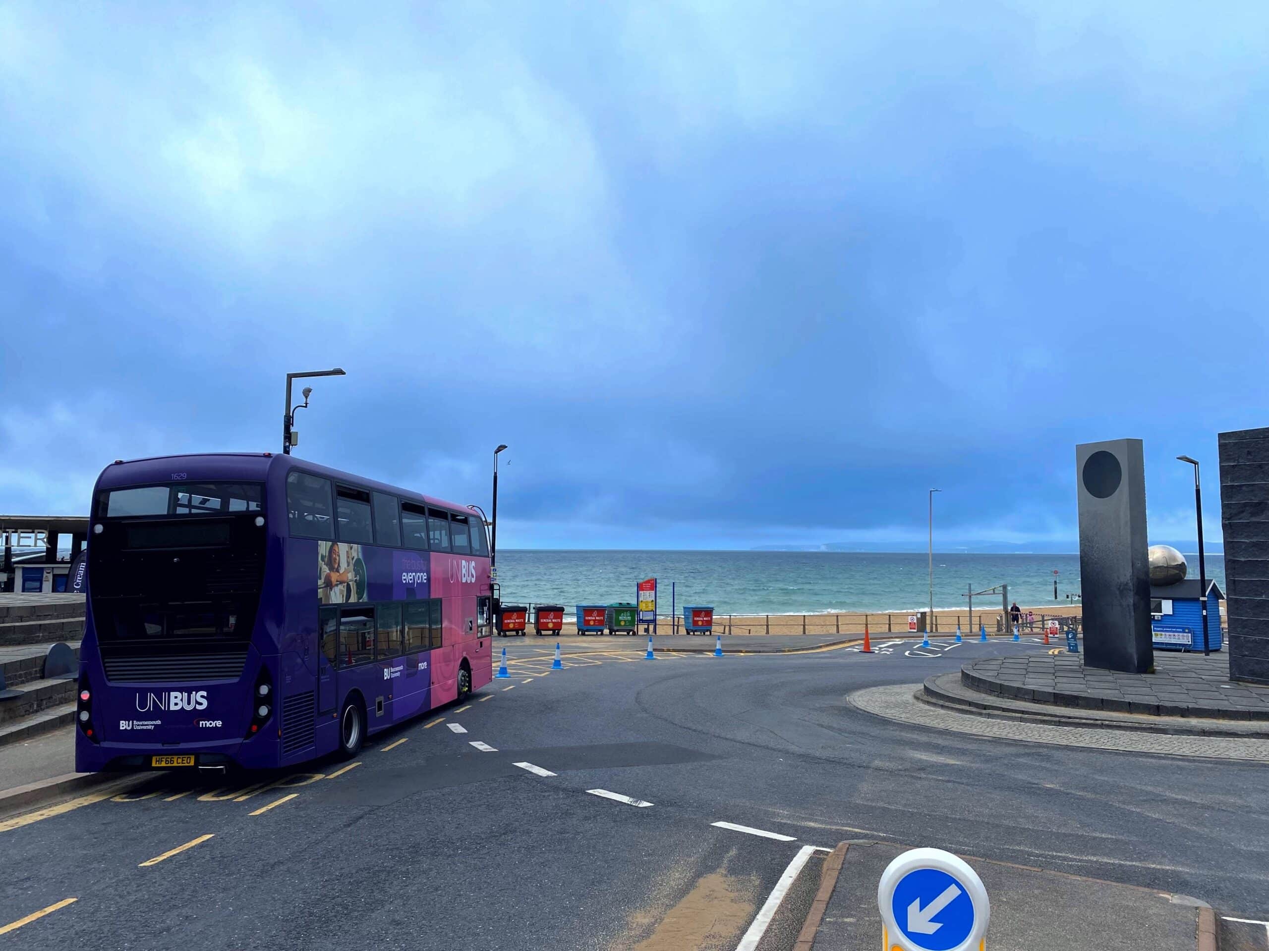 A double-decker bus at the bus stop next to Boscombe Pier in Bournemouth. A view of an empty beach and the sea are in the background.