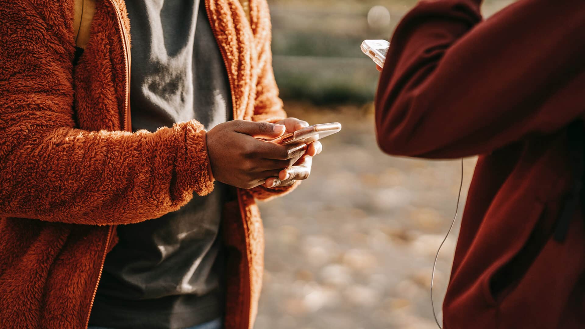 Close up of two people outside. Both are holding smartphones.