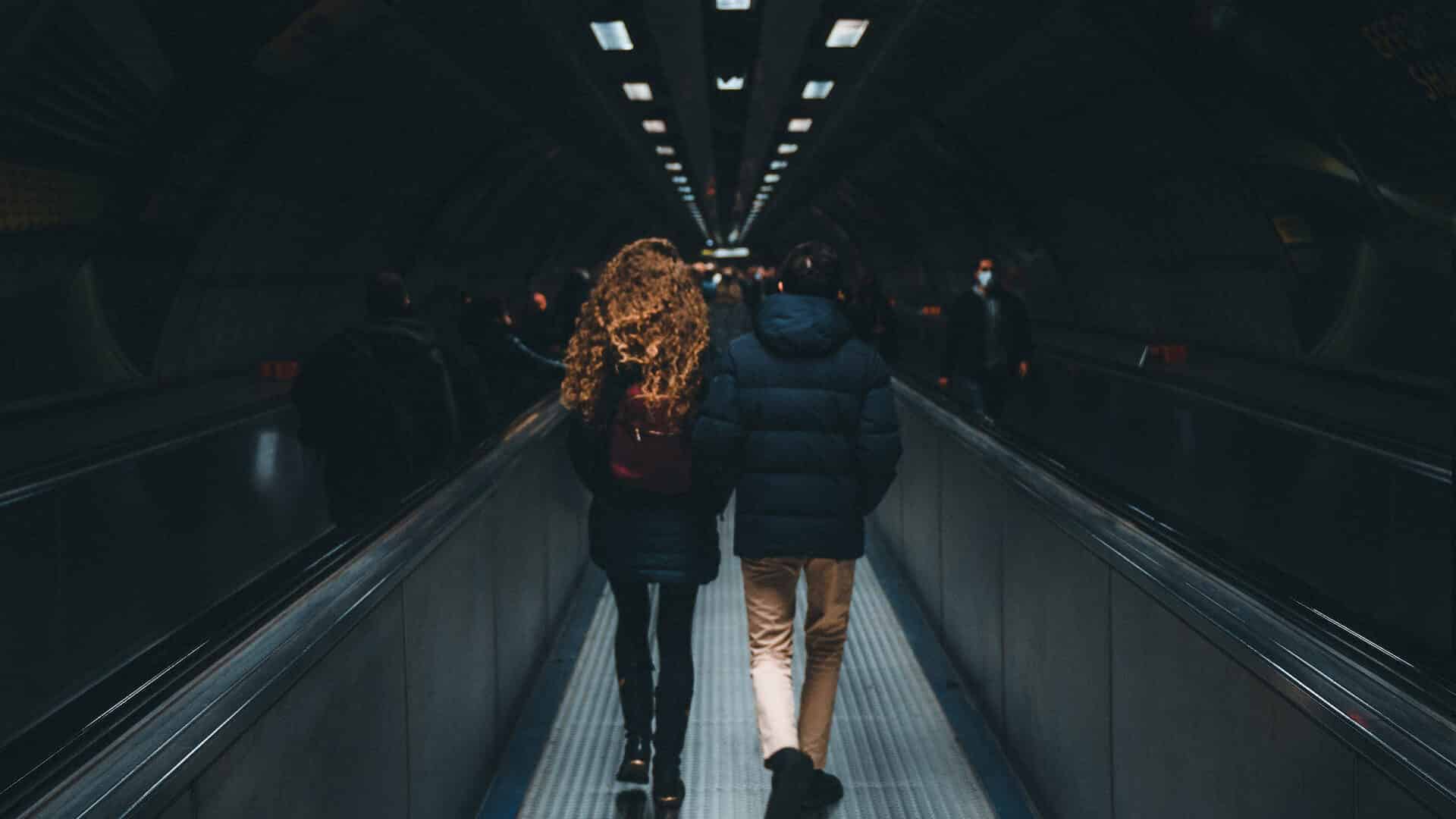 Two people seen from behind walking along an underground station tunnel