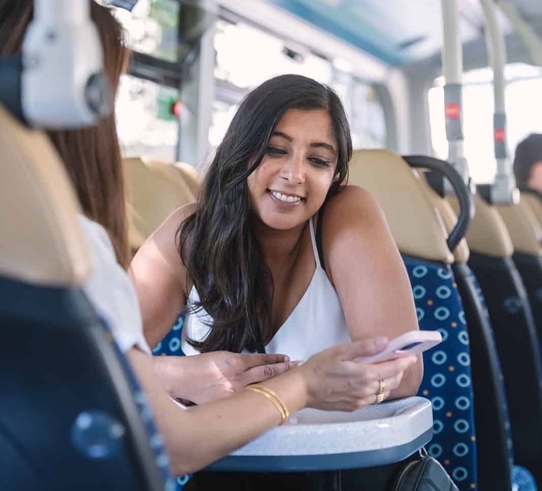 Woman sitting at a table on a bus looking at a phone being shown to her by another passenger